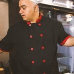 Chef in black uniform with white hat cooking in a restaurant kitchen in Louisville, KY.