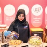 Female chef in hijab serves pastries at a stylish bakery in Islamabad, showcasing delectable treats.